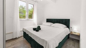A bedroom with a bed, a nightstand, a window with curtains, and a view of trees outside.