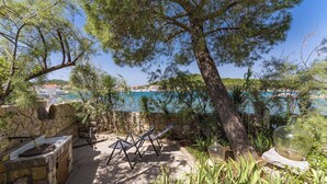 A stone-built outdoor area with a stone bench, a grill, and a view of the sea.