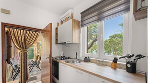 A modern kitchen with white cabinets, a stainless steel sink, and a window with a view of trees.
