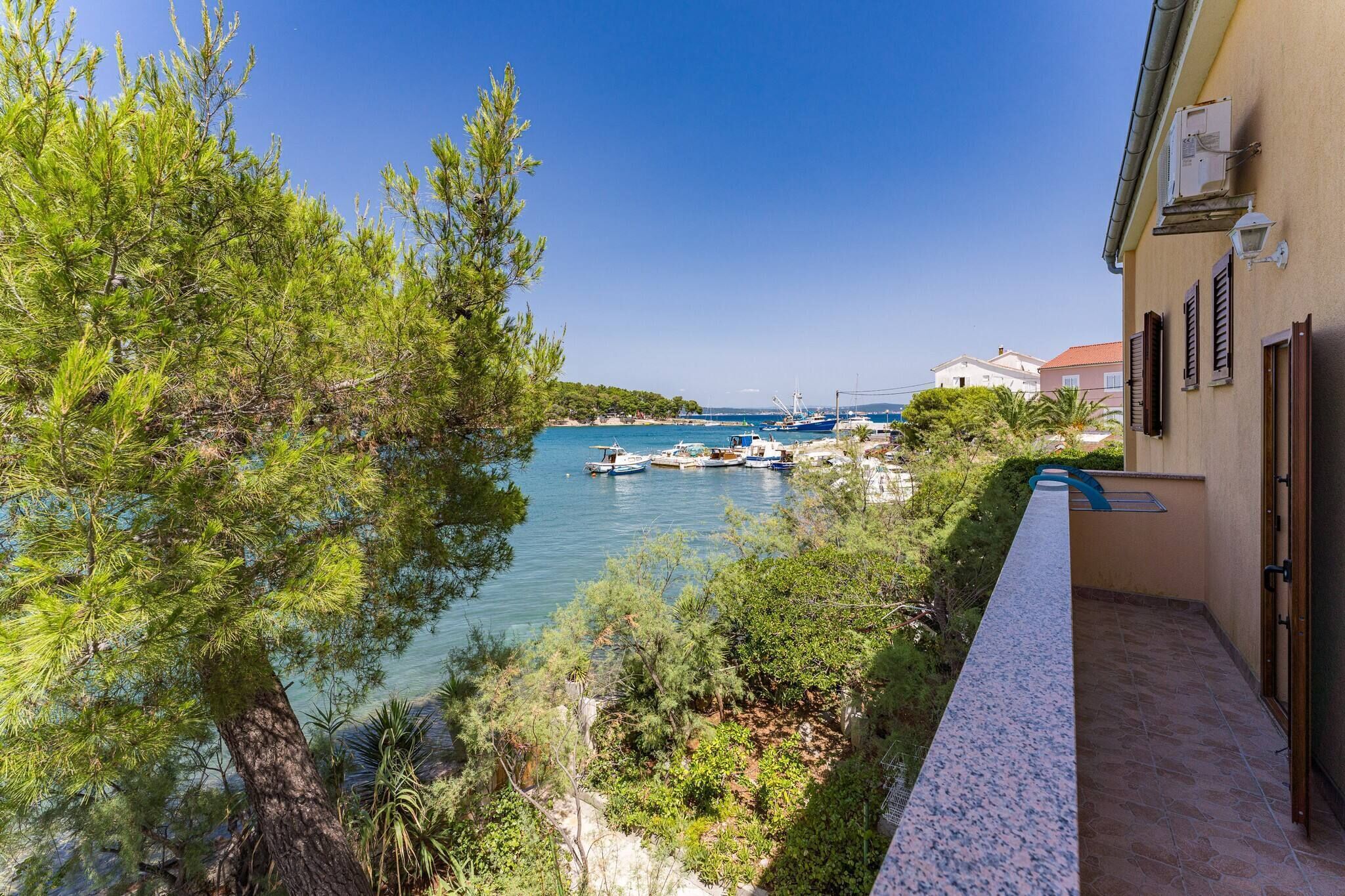 Blick auf die Küste mit vor Anker liegenden Booten, einem klaren Himmel und einem Gebäude mit einem Balkon mit Blick auf das Wasser.
