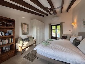 Een slaapkamer met een bed, een houten boekenkast, een bureau, een raam met gordijnen en een plafondventilator.