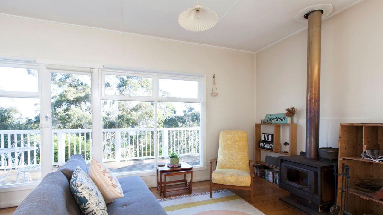 A living room with a sofa, a chair, a table, a bookshelf, a fireplace, and large windows.