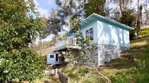 A light blue house with a balcony, surrounded by trees and a grassy area.
