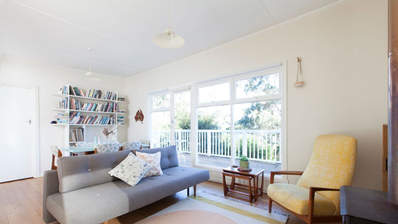A living room with a sofa, armchair, bookshelf, and a window with a view.