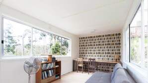 A room with a large window, a fan, a bookshelf, a desk, and a sofa. - Ipanema (Wye River)