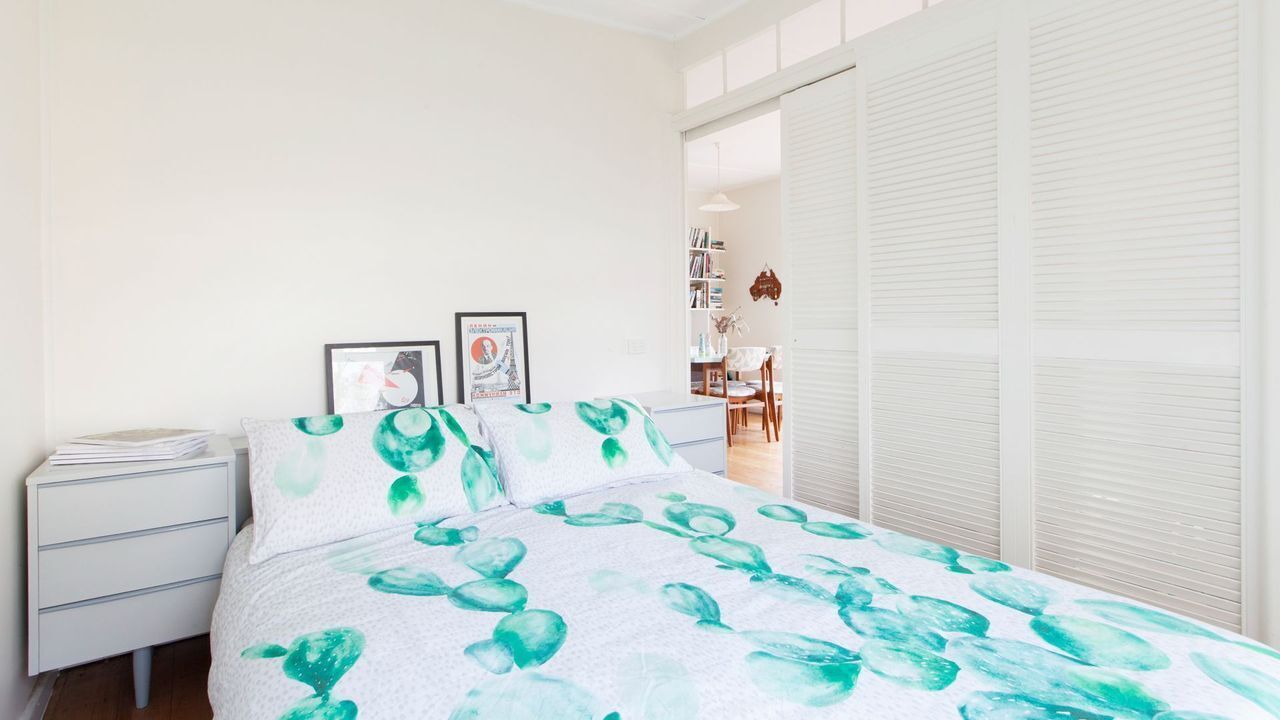 Een slaapkamer met een bed, nachtkastje en raam met jaloezieën.