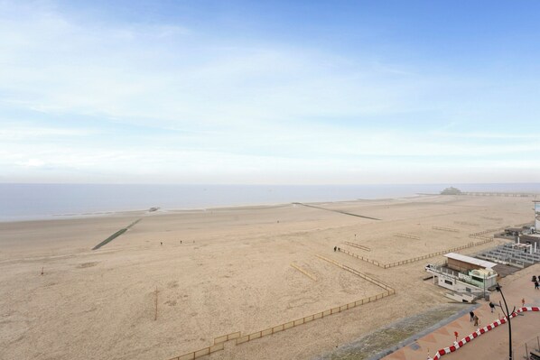 A wide sandy beach with a clear sky, a lifeguard tower, and a distant structure. - Apartment in Blankenberge With Sea Views (Blankenberge)