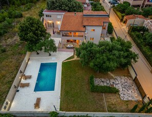 Uma casa de dois andares com piscina, um pátio com mobiliário externo e um jardim bem cuidado.