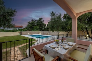 Área de pátio com piscina, mesa de jantar posta para quatro pessoas e vista para a piscina e vegetação ao redor.