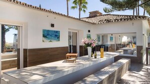 A modern reception area with a long reception desk, a painting of a beach scene, and a vase with pink flowers. - Modern Versace-themed Villa (Marbella)