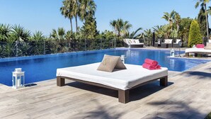 A poolside area with a lounge chair, a small table, and a bench with towels. - Modern Versace-themed Villa (Marbella)
