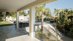 A modern outdoor area with a glass enclosure, a pool, and a staircase leading to a covered terrace. - Modern Versace-themed Villa (Marbella)