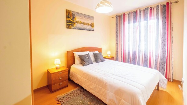 Una camera da letto con un letto, comodini, una lampada, un quadro e una finestra con tende.