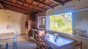Zona pranzo con tavolo e sedie in legno, camino in mattoni e un'ampia finestra vista verde.