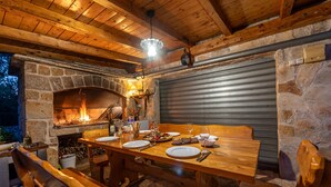 Ein rustikaler Essbereich im Freien mit Kamin aus Stein, Holzbänken und einem Tisch, gedeckt für eine Mahlzeit.