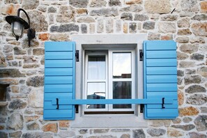 Traditional stone building with a charming window featuring shutters and a wall-mounted light.