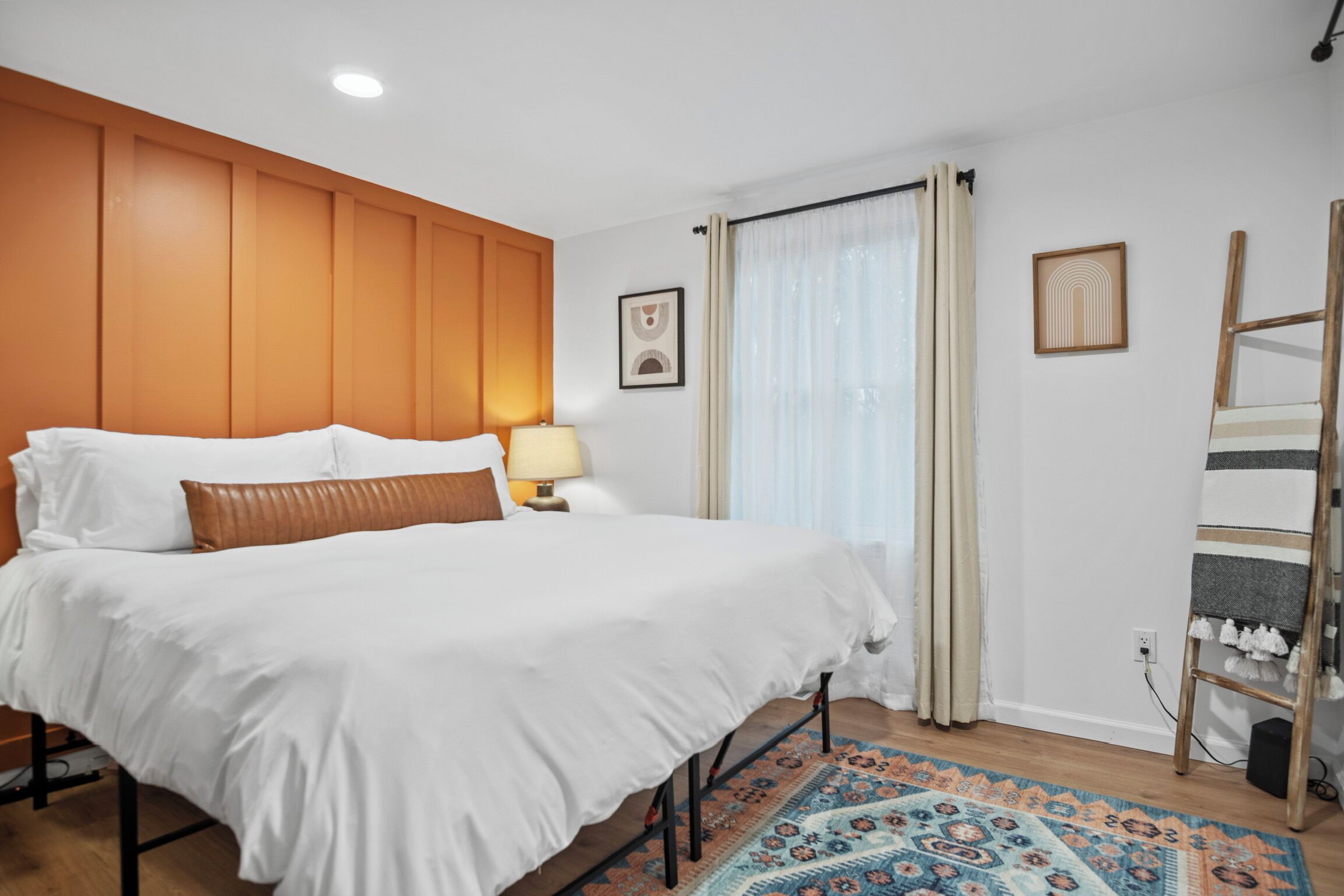 Hotelkamer met een groot bed, een houten hoofdbord, een nachtkastje met een lamp, een kamerbreed tapijt met een patroon, en een raam met gordijnen.