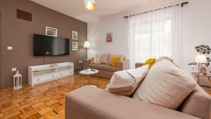Ein Wohnzimmer mit einer Couch, einem Fernseher, einer Lampe und einem Fenster mit Vorhängen.