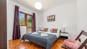 Ein Schlafzimmer mit Holzboden, einem Bett mit blauer Steppdecke, einem rosa Sessel und einem Bild an der Wand.