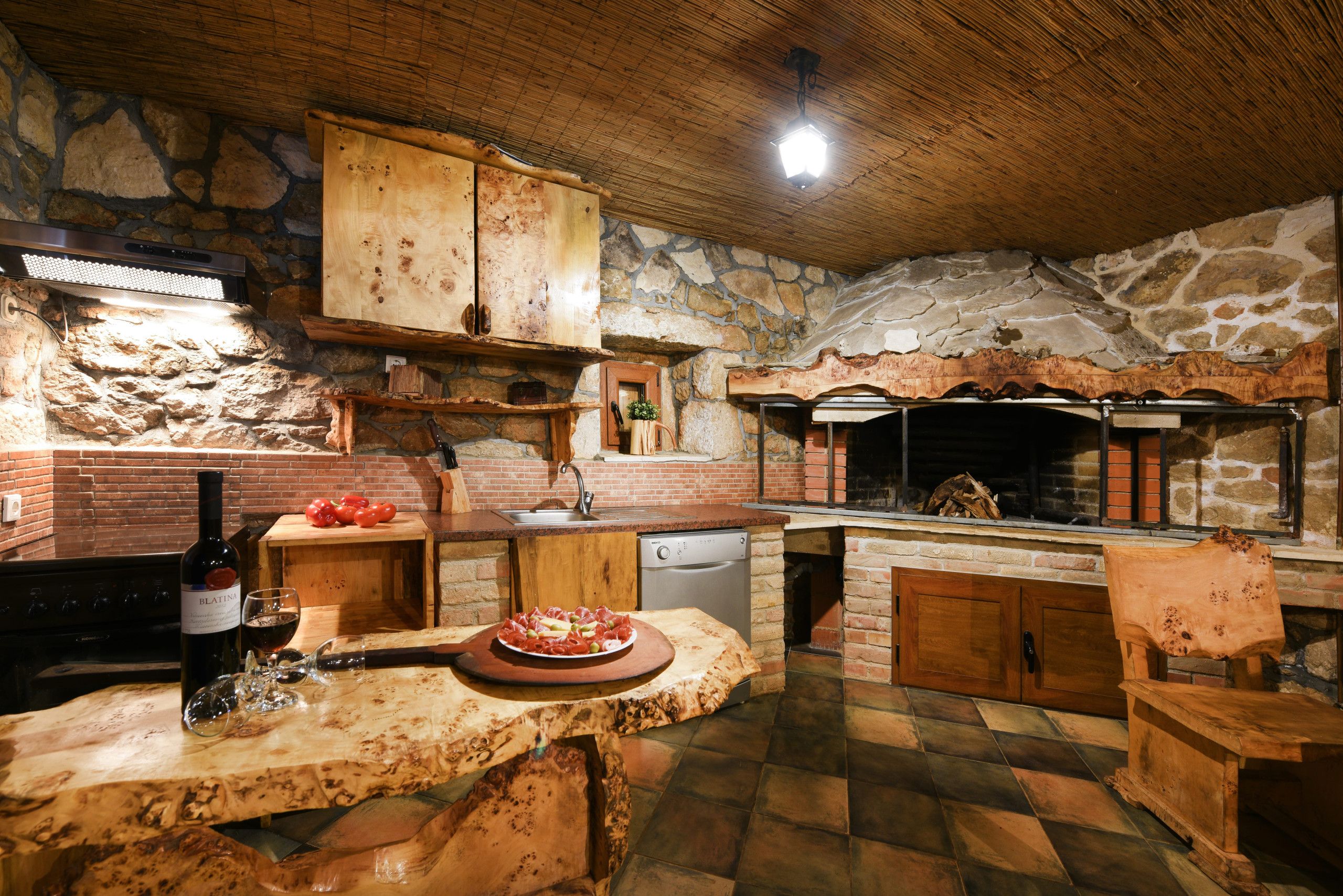 A rustic kitchen with a stone wall, wooden cabinets, a built-in oven, and a dining area with a wooden table.