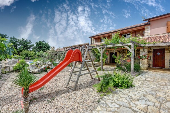 A residential property with a stone patio, a red slide, and a wooden pergola with climbing plants. - Villa Smilje ZadarVillas (Slivnica)