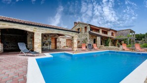 Area piscina con edifici in pietra, piscina azzurra e lettini da relax.