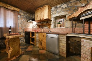 A rustic kitchen with a stone wall, wooden cabinets, and a built-in dishwasher. - Villa Smilje ZadarVillas (Slivnica)