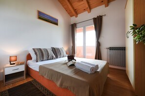 Un dormitori amb un llit, una tauleta de nit, una làmpada, una finestra amb cortines, un radiador i un quadre a la paret.