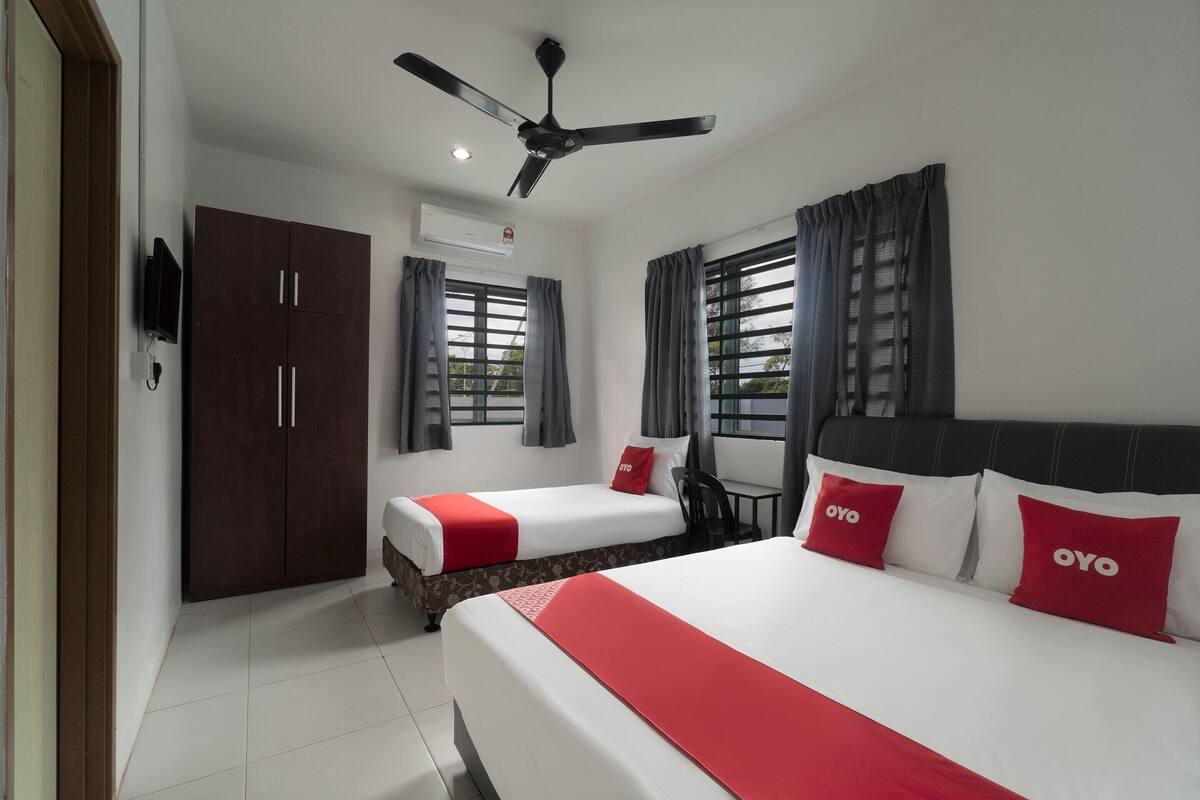 Une chambre d’hôtel avec deux lits, une armoire, un ventilateur de plafond et une fenêtre avec des rideaux.