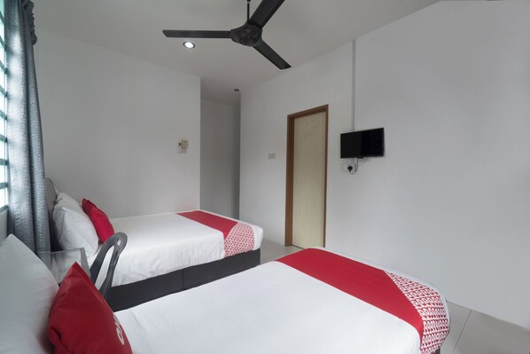 A hotel room with two beds, a ceiling fan, a TV mounted on the wall, and a door.