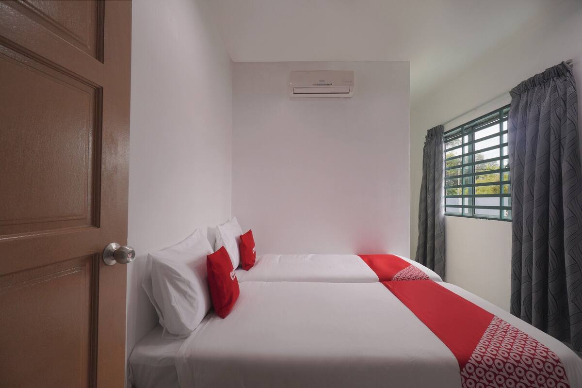 Une chambre d’hôtel avec deux lits, une fenêtre avec des rideaux, un appareil de climatisation et une porte en bois.
