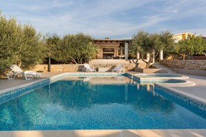 Piscina con sillas de descanso, pared de piedra y zona exterior cubierta con una parrilla.