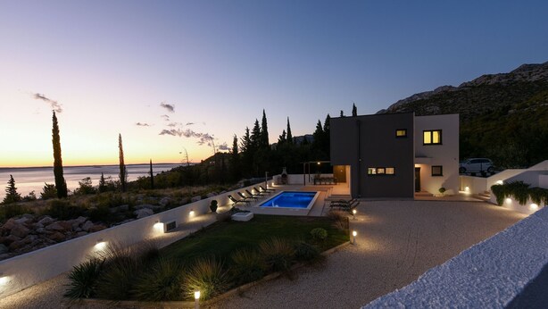 A modern house with a swimming pool, surrounded by a landscaped garden and a view of the sea.