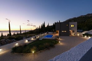 A modern house with a swimming pool, surrounded by a landscaped garden and a view of the sea.