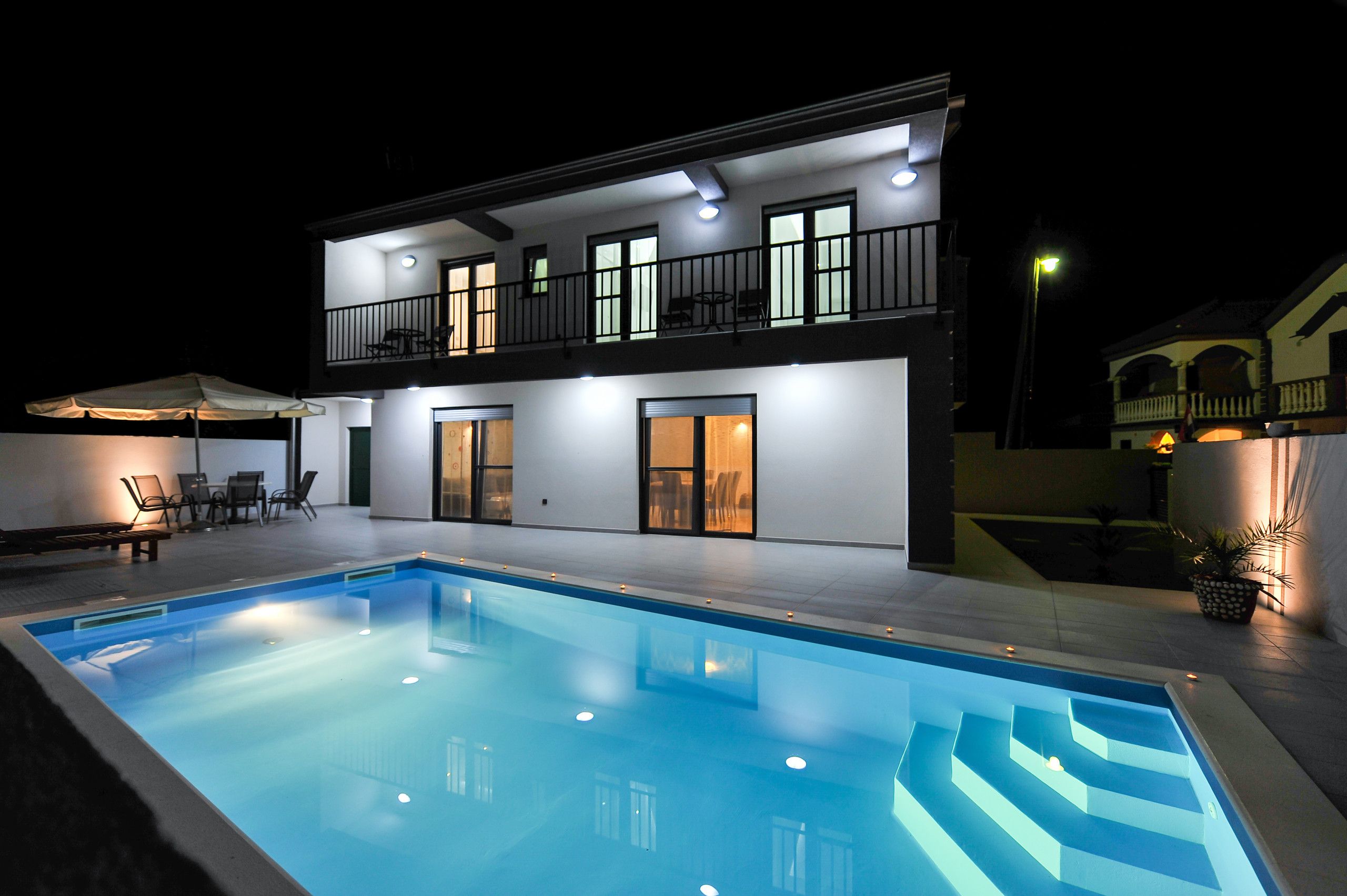 Une maison à deux étages avec une piscine, un espace salon extérieur et un balcon.