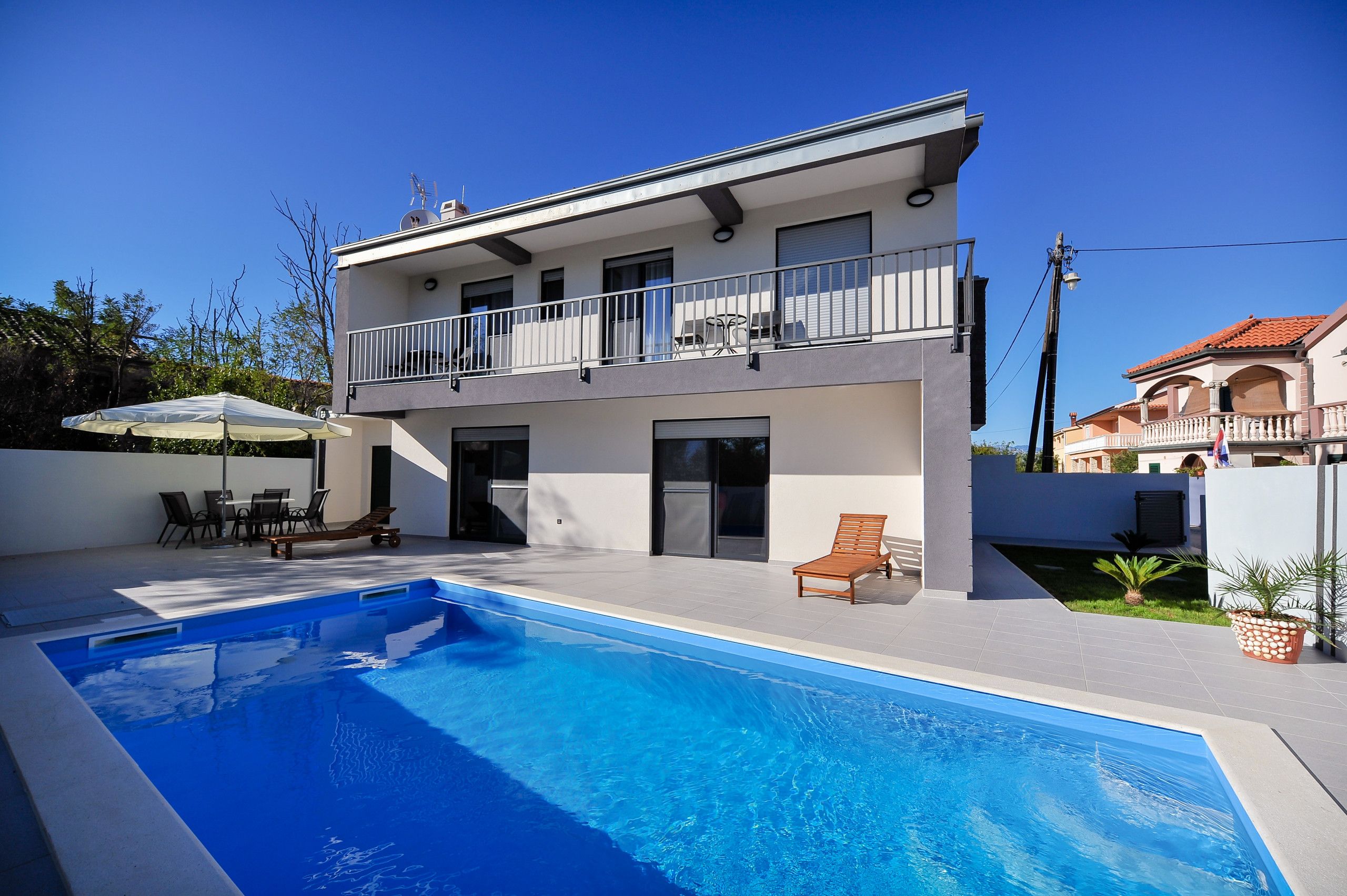 A modern two-story house with a swimming pool, outdoor furniture, and a balcony.