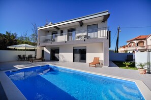 Une maison moderne à deux étages, dotée d’une piscine, de mobilier d’extérieur et d’un balcon.
