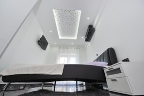 A modern bedroom with a bed, bedside storage, a ceiling light fixture, and a window with curtains.