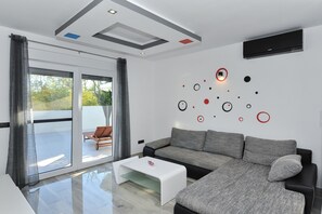 Uma sala de estar moderna com um sofá cinzento, uma mesa de centro branca e um amplo painel de vidro deslizante que dá para uma área externa.