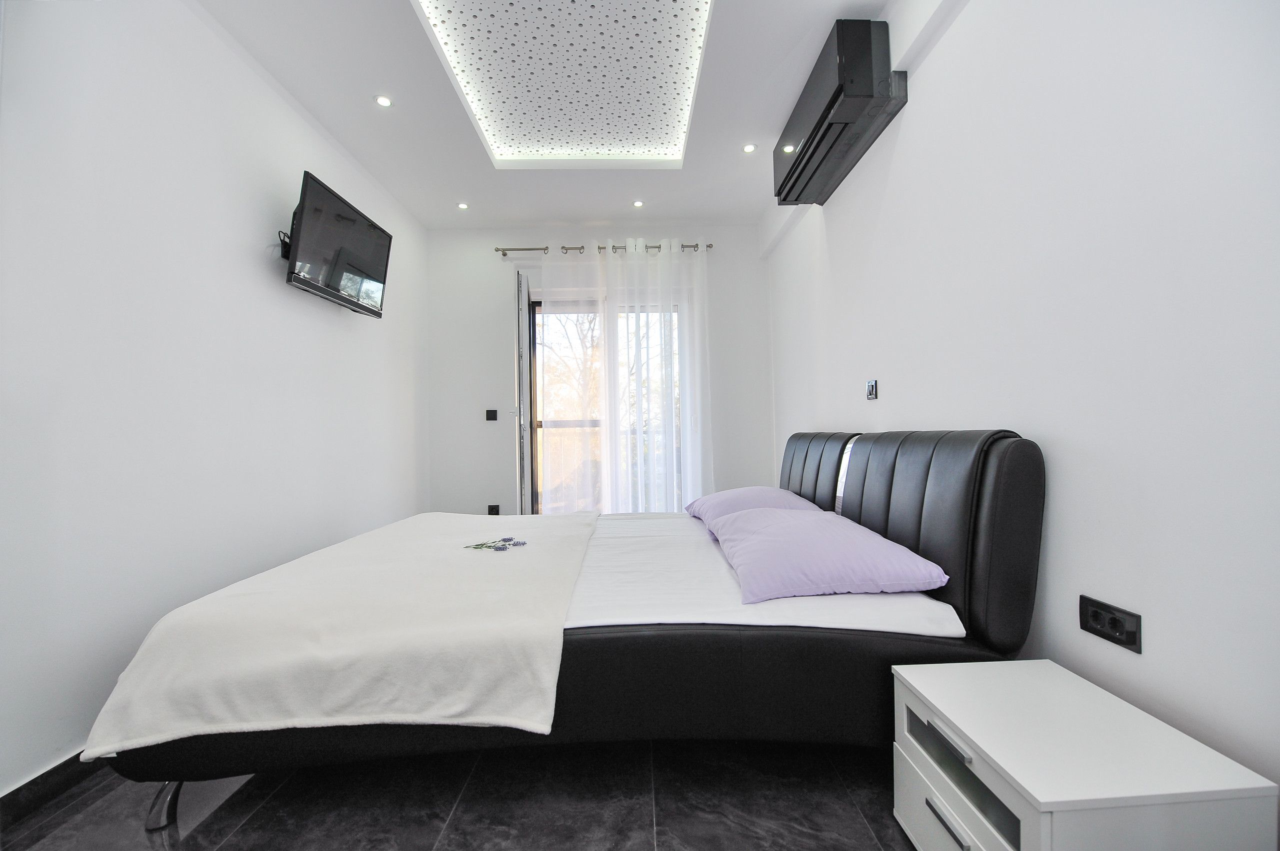 Un dormitorio moderno con una cama, un televisor montado en la pared y una lámpara en el techo.