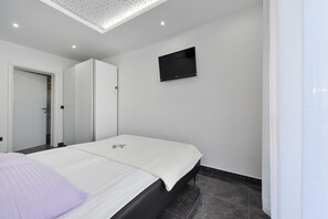 Une chambre moderne avec un lit, un téléviseur à écran plat fixé au mur et une porte donnant accès à une salle de bain.