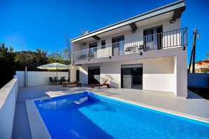 Une maison à deux étages avec une piscine, du mobilier d’extérieur et un balcon.