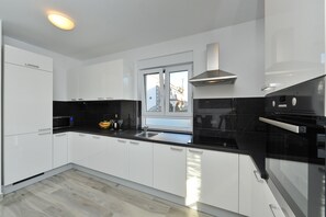 A modern kitchen with white cabinets, a black countertop, a stainless steel range hood, and a window with a view of buildings outside.
