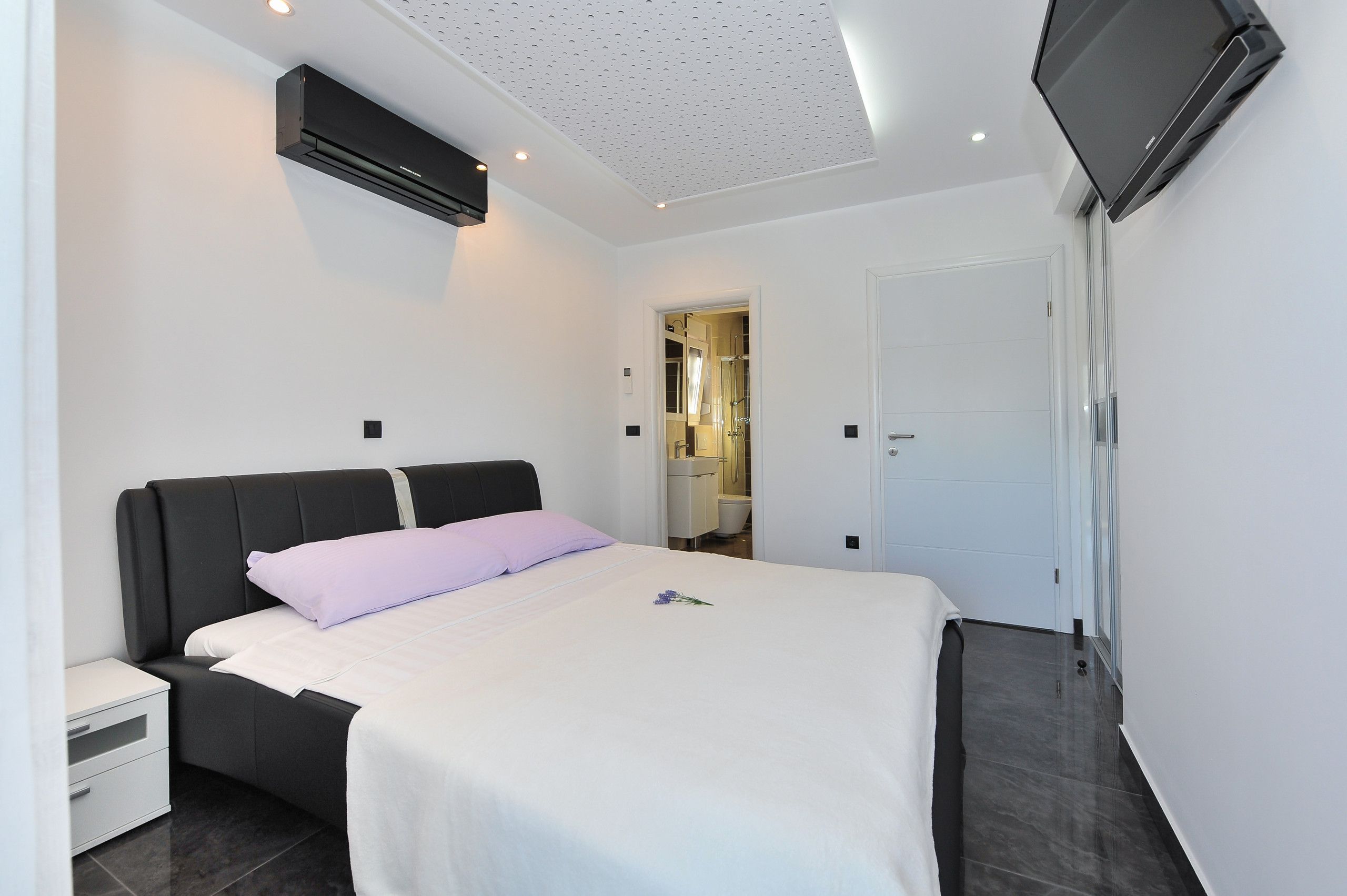 Ett modernt hotellrum med en säng, ett sängbord, en platt-TV som är monterad på väggen och en luftkonditioneringsanläggning.
