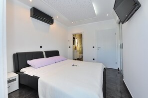 Une chambre d’hôtel moderne équipée d’un lit, d’une table de chevet, d’un téléviseur à écran plat fixé au mur et d’un appareil de climatisation.