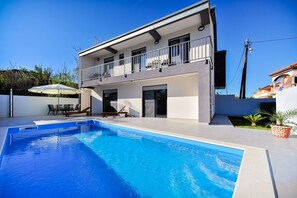 Une maison à deux étages avec une piscine, du mobilier d’extérieur et un balcon.