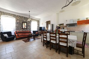 A living room with a sofa, a dining table with chairs, a kitchen area with a stove, and a stone wall.