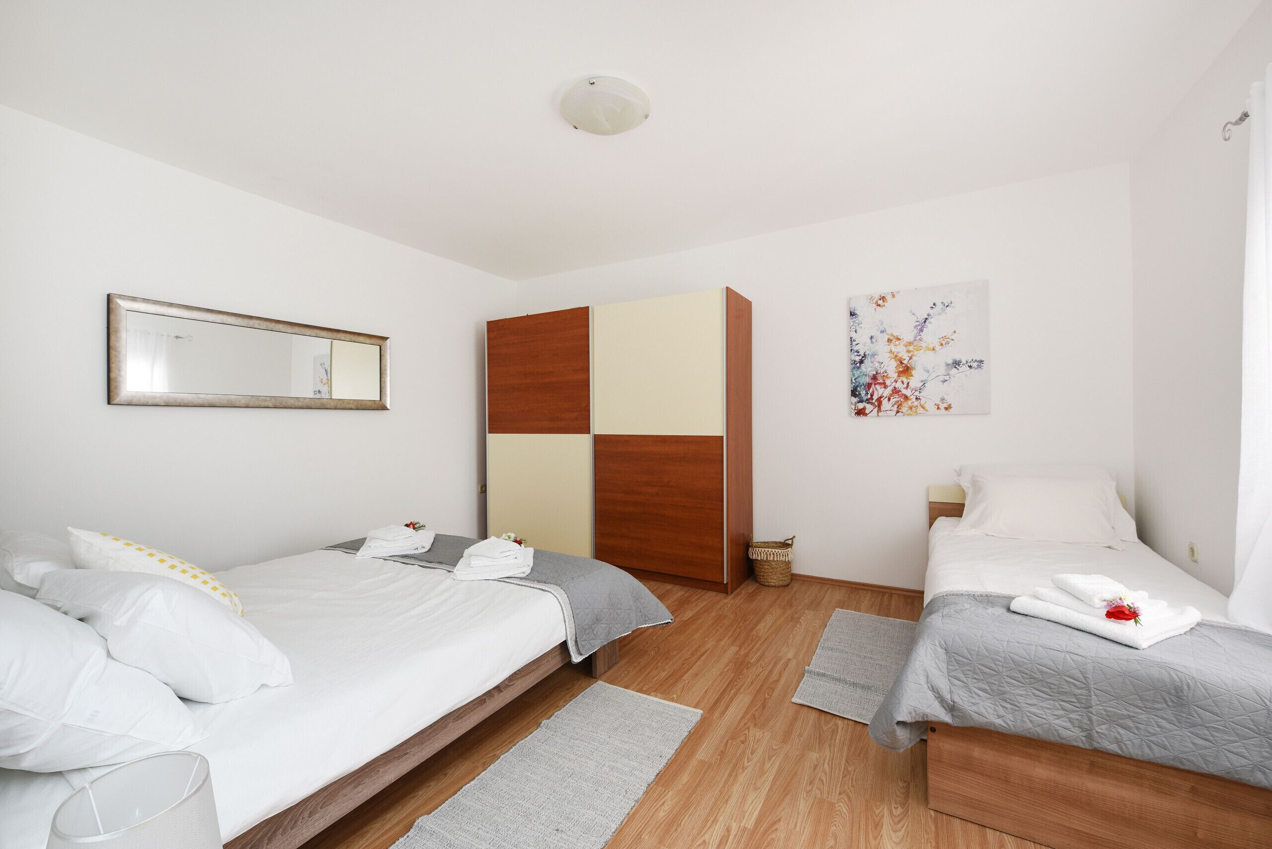 Een moderne hotelkamer met twee bedden, een garderobe, een spiegel en een schilderij.
