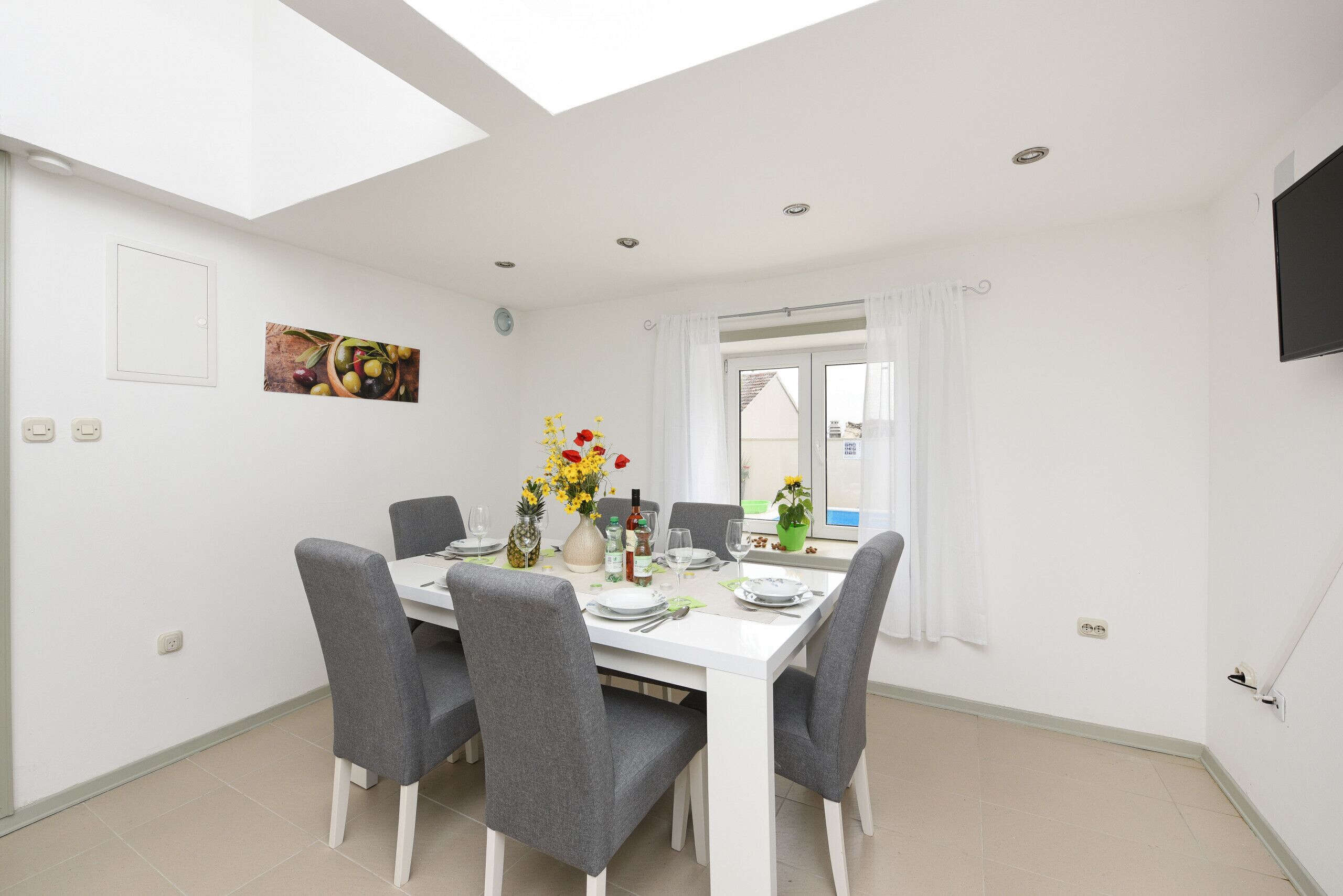 Un coin repas avec une table blanche, des chaises grises et un vase à fleurs.
