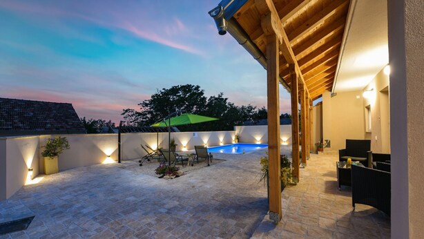 Un espacio al aire libre techado con piscina, mobiliario y una iluminación ambiental.